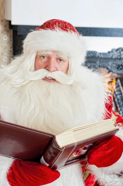 Santa zitten op de kerstboom, open haard en het lezen van een boo — Stockfoto