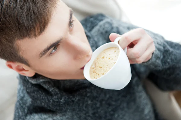 Portræt af en ung mand drikker kaffe, mens han sidder på armchai - Stock-foto