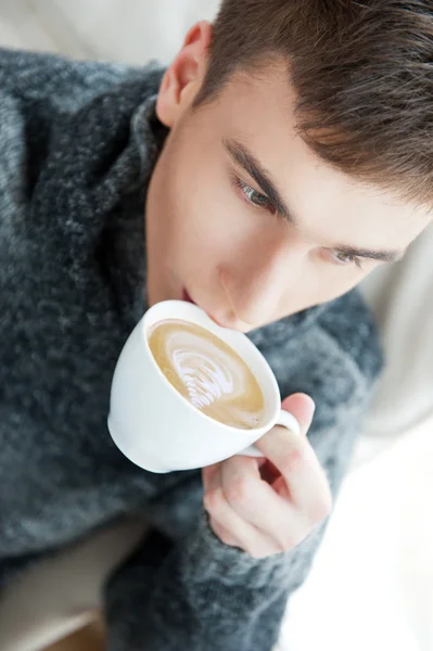 Portrait of a young man drinking coffee while sitting on armchai — Stock Photo, Image