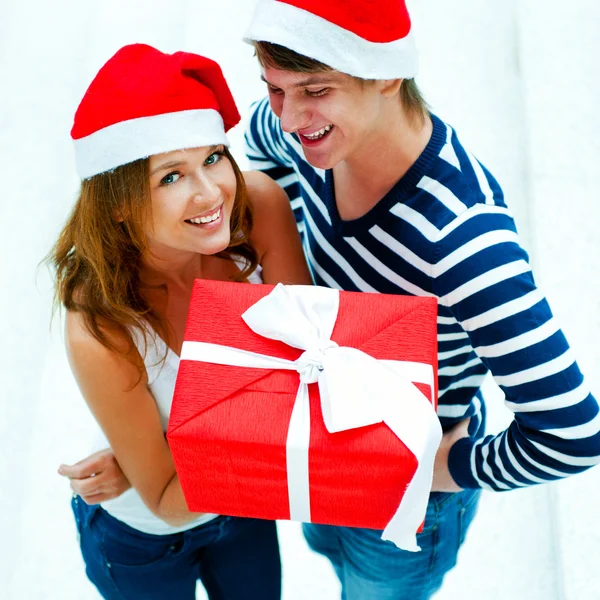 Jovem casal feliz em chapéus de Natal de pé juntos e holdi Fotografia De Stock
