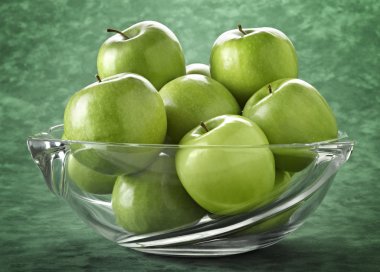 Glass bowl filled with green apples on green background clipart