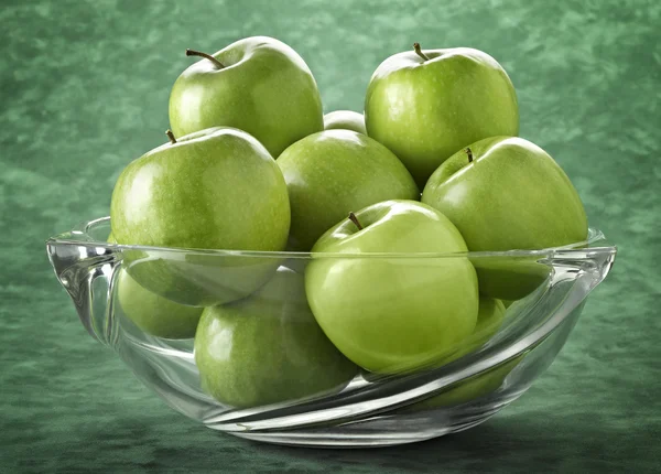 Glass bowl filled with green apples on green background Royalty Free Stock Photos