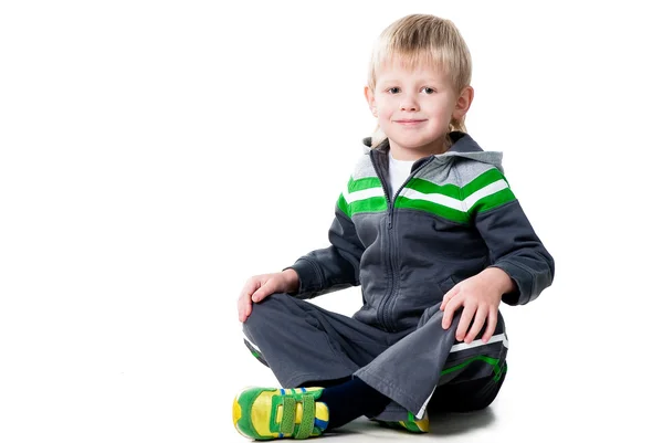 Счастливый спортивный мальчик, сидящий на полу в изоляции на белом фоне — стоковое фото