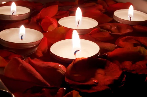 Röda kronblad av rosor och små ljus i vatten — Stockfoto