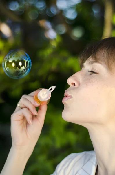 Beautiful young woman inflating soap bubbles outdoors — Stock Photo, Image