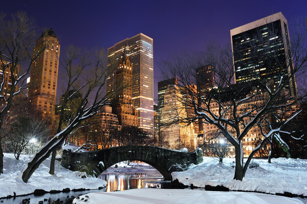 New York City Manhattan Central Park panorama in winter with snow, bridge, freezing lake and skyscrapers at dusk.