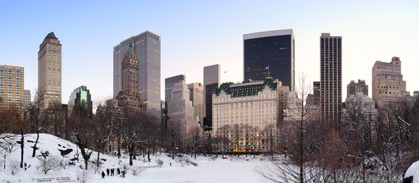 New York City Manhattan Central Park panorama in winter with snow, freezing lake and skyscrapers at dusk.