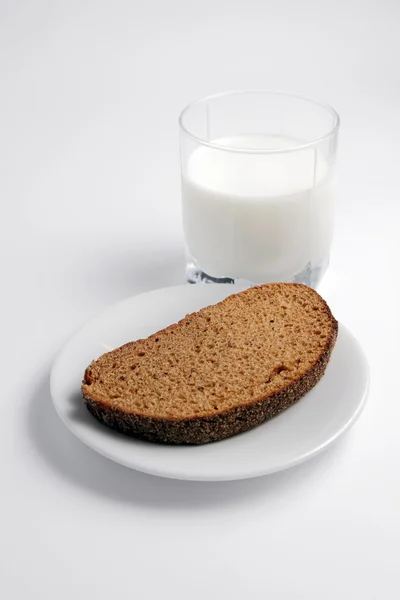 Kawałek czarnego chleba, szklanka mleka na białej talerzu. — Zdjęcie stockowe