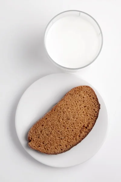 En bit svart bröd, ett glas mjölk på en vit tallrik. — Stockfoto