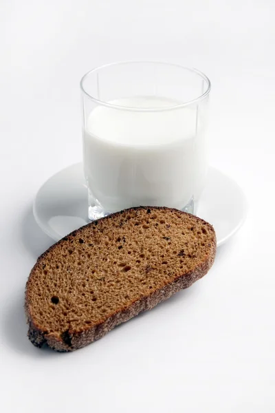 Un pezzo di pane nero, un bicchiere di latte su un piatto bianco . — Foto Stock