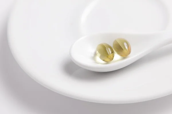 stock image Fish oil capsules on a white saucer in white spoon.