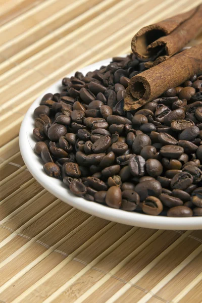 Koffie bonen met buizen van kaneel op een witte schotel — Stockfoto