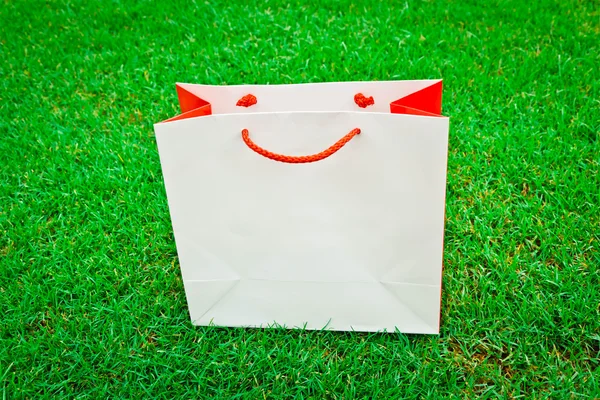 緑の芝生の上に白の赤いショッピング バッグ — ストック写真