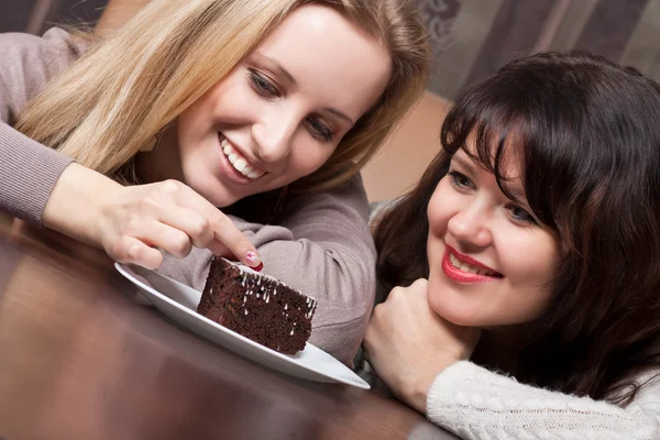 Dos hermosas chicas sonrientes comiendo un pastel — Foto de Stock