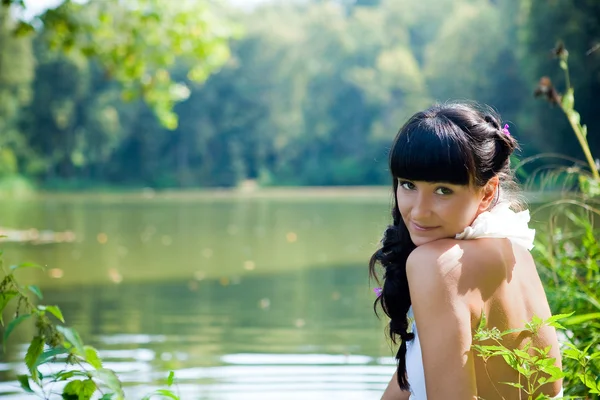Молодая сексуальная брюнетка сидит у реки — стоковое фото