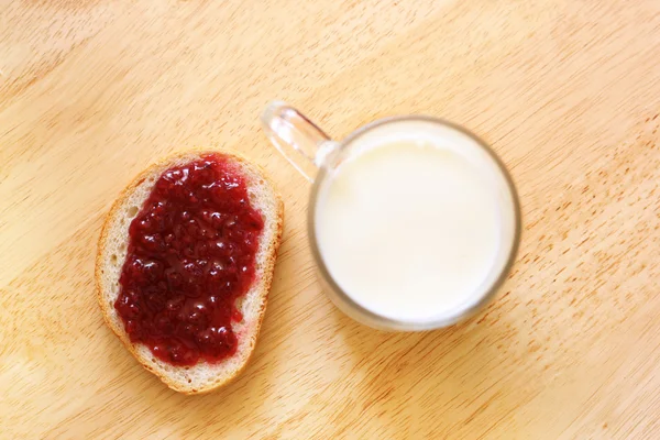 Хліб з джемом і склянкою молока на дерев'яному столі — стокове фото