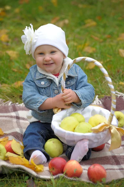 Den lille jenta sitter med en kurv med epler. – stockfoto