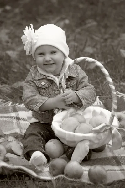 Den lille jenta sitter med en kurv med epler. – stockfoto