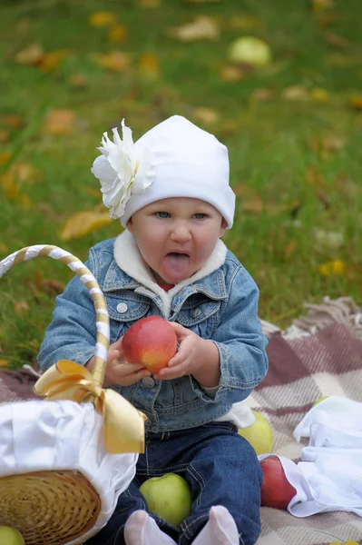 Lille pige sidder med en kurv af æbler - Stock-foto