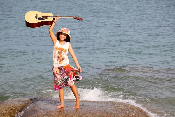 ビーチそばの石のギターを持つかなり若い女性 — ストック写真