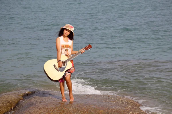 Pretty young woman with guitar on stone near beach — Stock Photo, Image