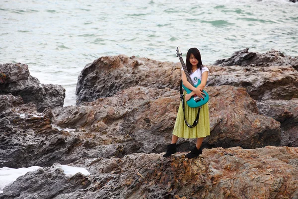 Beautiful asian woman with a guitar on rock — Stock Photo, Image