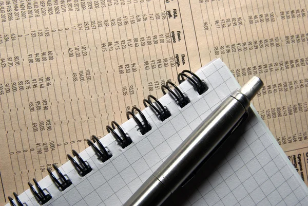Stift und Notizbuch auf Zeitung mit Finanzdaten. — Stockfoto