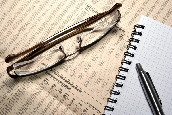 Glasses, pen and notebook laying on newspaper with financial num — Stock Photo, Image