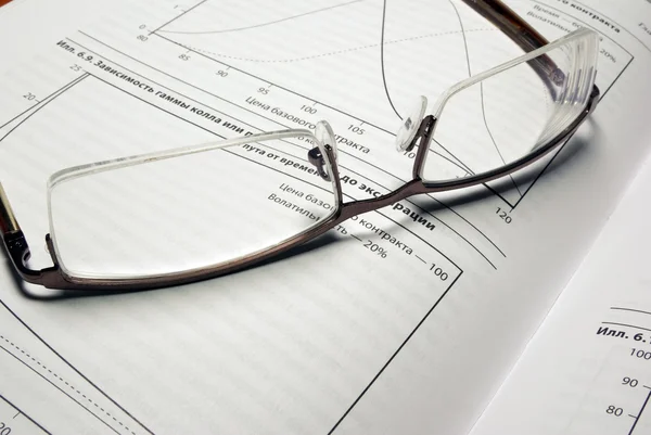 Glasses laying on book with financial charts. — Stock Photo, Image