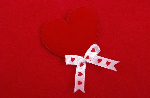 Red heart with silk ribbons isolated on red textured background. — Stock Photo, Image