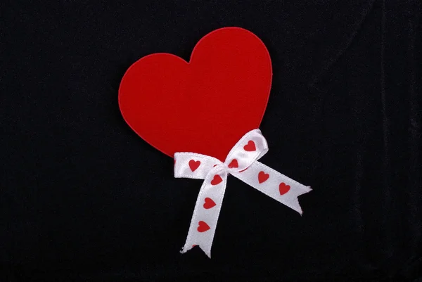 Red heart with white ribbons isolated on black velvet background — Stock Photo, Image
