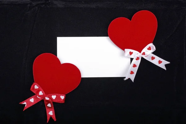 Twee rode harten en witte kaart geïsoleerd op fluweelzwart pagina — Stockfoto