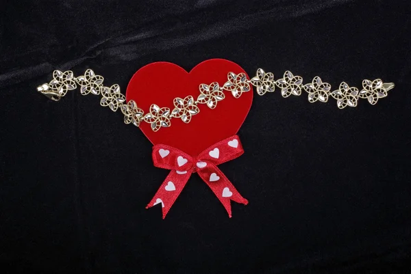 Золотой браслет с красным сердцем, изолированным на черном бархатном заднем плане — стоковое фото