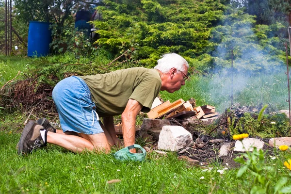 Senior man trying to make a bonfire — Stock Photo, Image