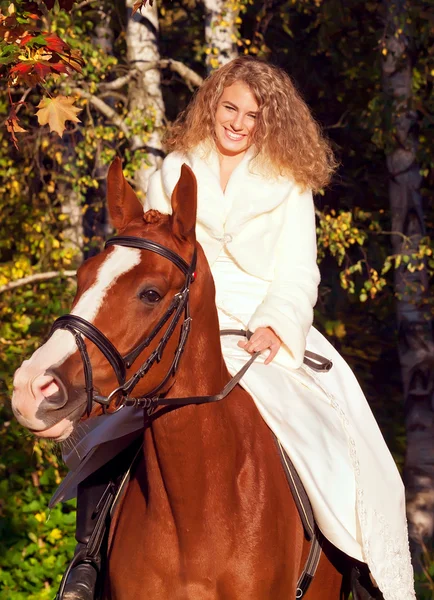 Smiling young bride sitting on horse in forest — Stock Photo, Image