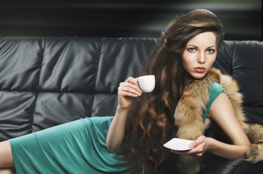 Young elegant girl in green with cup, she is lying on the sofa clipart