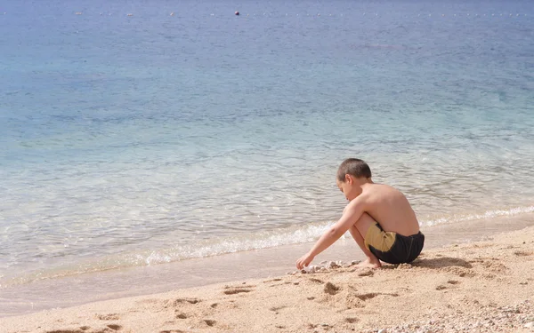 깨끗 한 빈 해변에 돌 멩이가지고 노는 어린 소년 — 스톡 사진