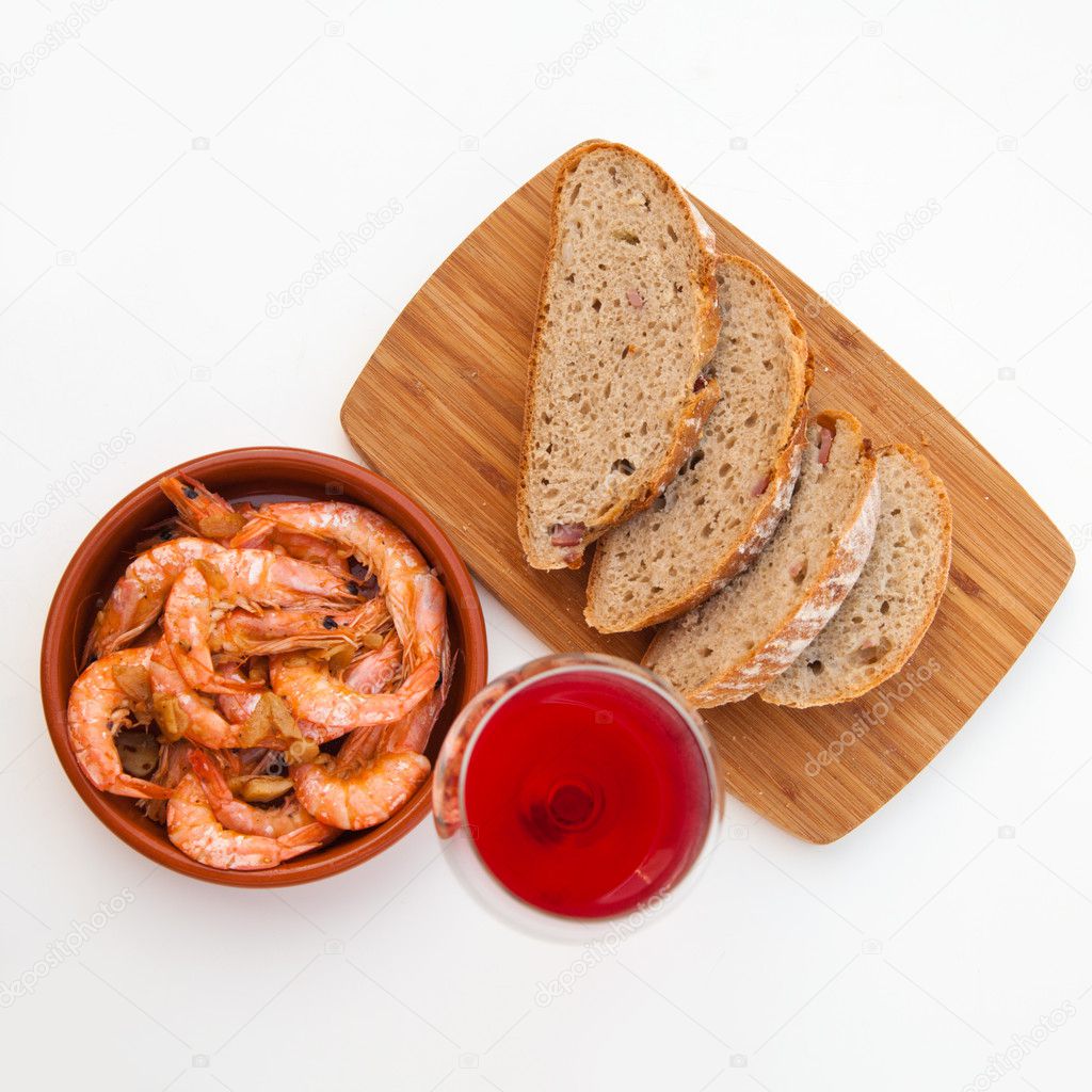 Garlic prawns in a terracotta dish, bread on a wooden board and