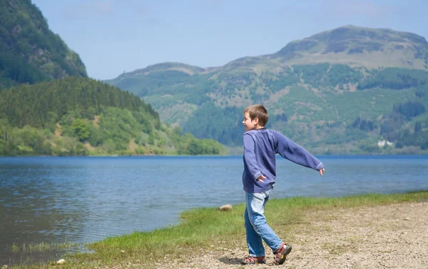 Liten pojke kastar stenar i vattnet, loch lubnaig — Stockfoto