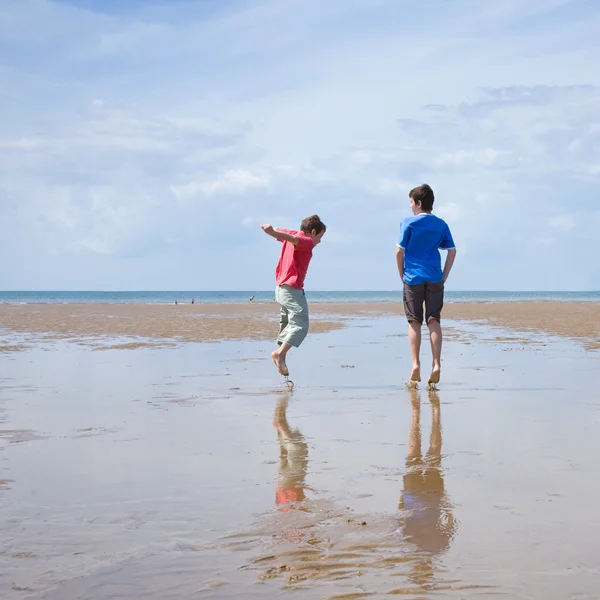 Due ragazzi che cercano di vedere chi farà una spruzzata più grande in bassa marea — Foto Stock