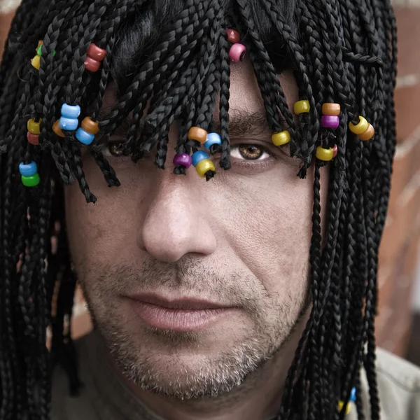 Caucasian guy in a party wig with many braids and beads — Stock Photo, Image
