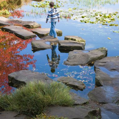 Little by in a stipy jumper is walking on the stepping stones clipart