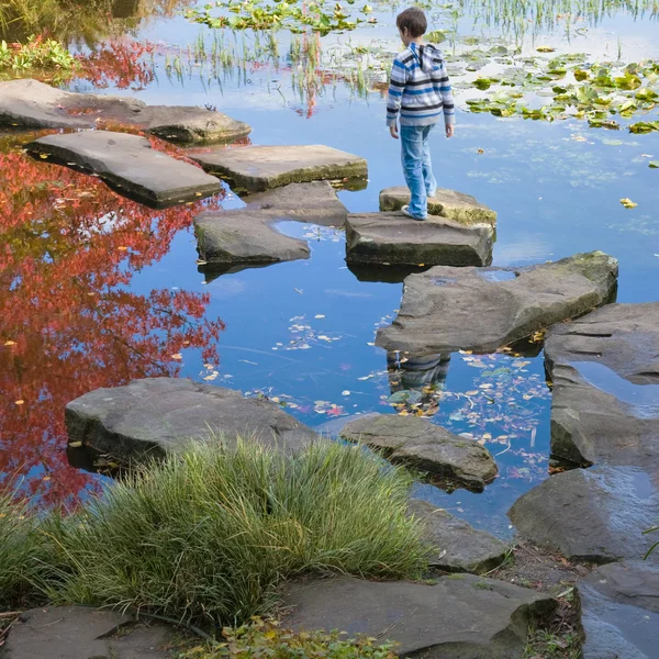 Little by in a stipy jumper is walking on the stepping stones — Stock Photo, Image
