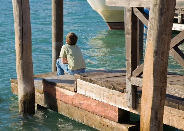 Kleine jongen zitten in de zon op een houten pier in Venetië; Italië — Stockfoto