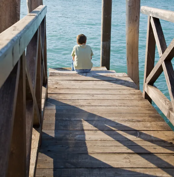 小男孩坐在一个木制的码头，在威尼斯; 上晒太阳意大利 — 图库照片