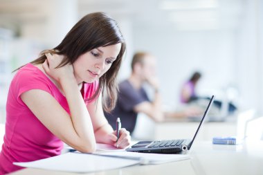 In the library - pretty female student with laptop and books clipart