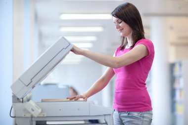 Pretty young woman using a copy machine clipart