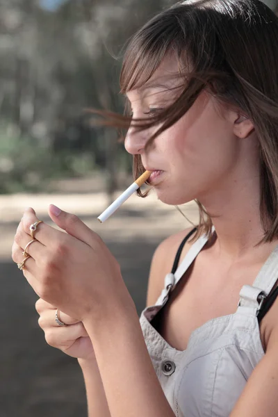 Retrato de uma jovem bonita acendendo um cigarro ao ar livre — Fotografia de Stock