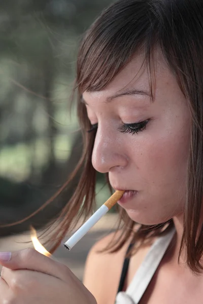 Portrait of a pretty young woman lighting a cigarette outdoors — Stock Photo, Image