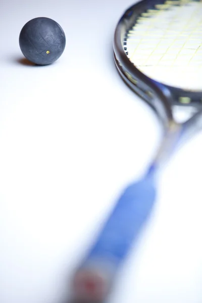 Pelota de squash y una raqueta de squash sobre fondo blanco — Foto de Stock